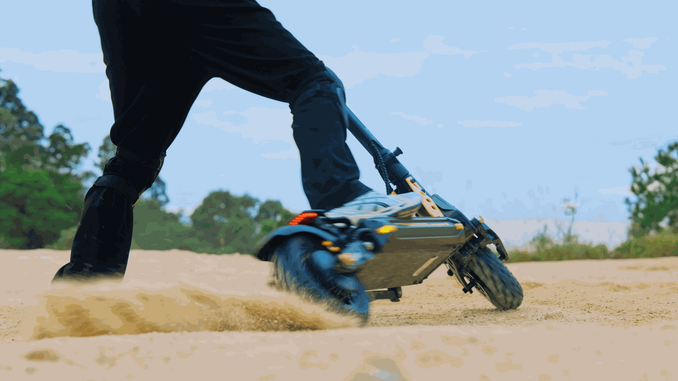 Person riding an off-road electric scooter with chunky tires on sandy terrain kicking up dust.