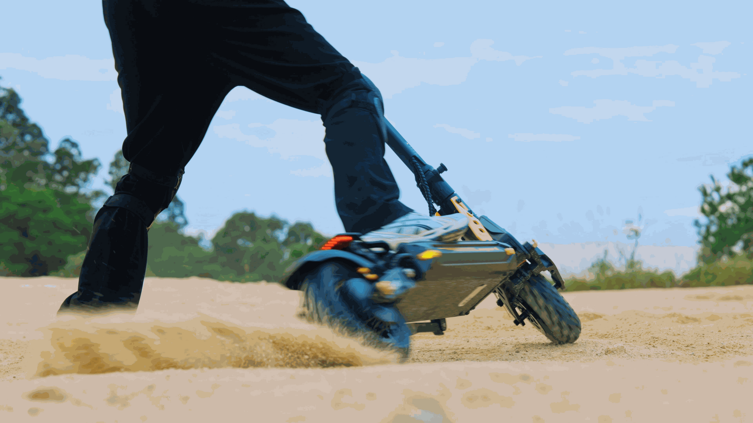 Person riding an off-road electric scooter with chunky tires on sandy terrain kicking up dust.
