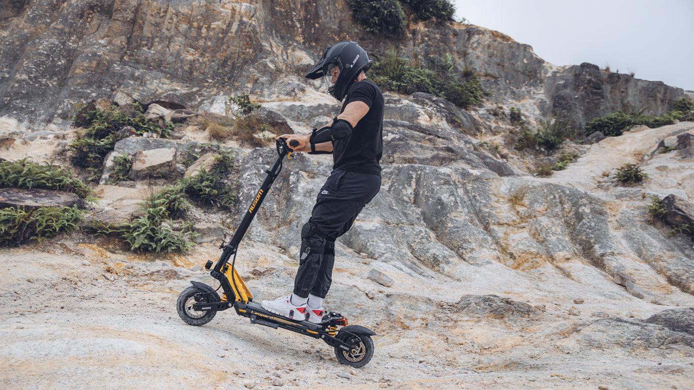 Man riding a yellow off-road electric scooter on rocky terrain with protective gear for a smooth e-scooter ride.
