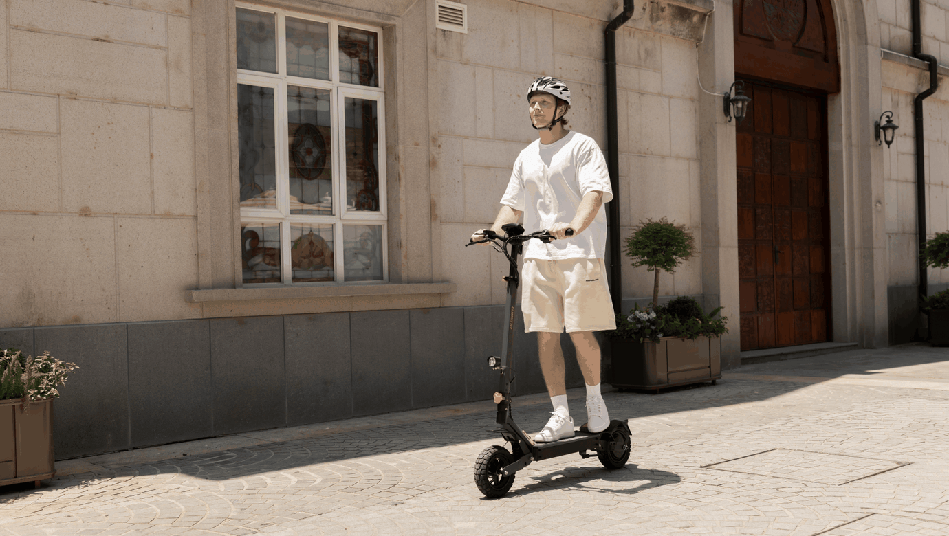 Man riding Ausom L1 electric scooter on a sunny urban street wearing helmet and casual summer clothes